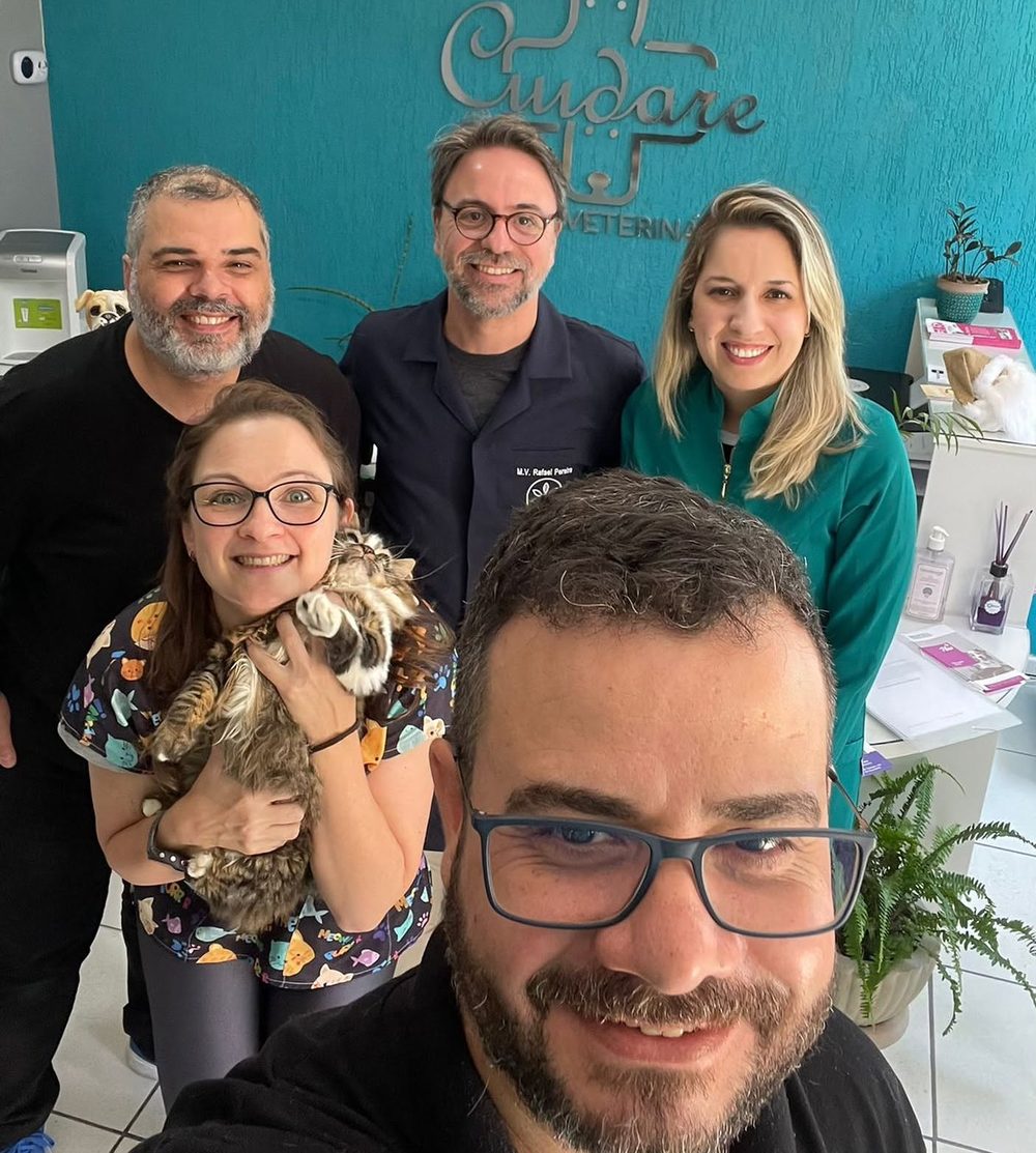 A equipe da Clínica Veterinária CUIDARE reunida na recepção, diante da parede turquesa com o logo, uma das veterinárias segurando um gato no colo