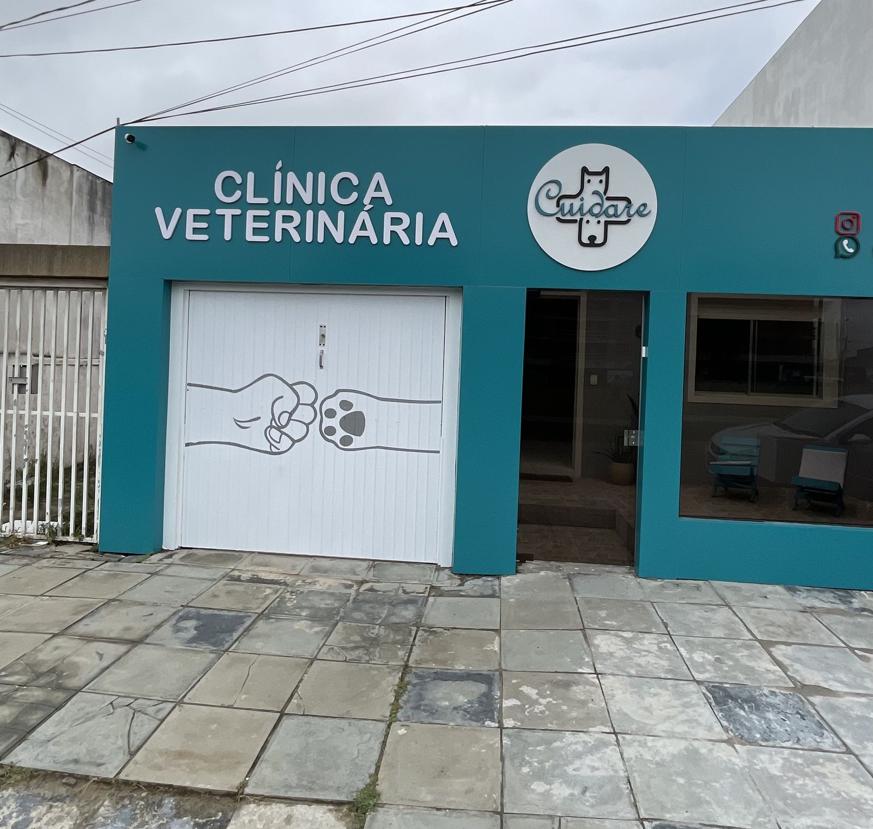 Fachada turquesa da Clínica Veterinária CUIDARE, na Av. Atlântica, no Cassino, com o logo da clínica e o desenho de um punho encostando numa patinha no portão