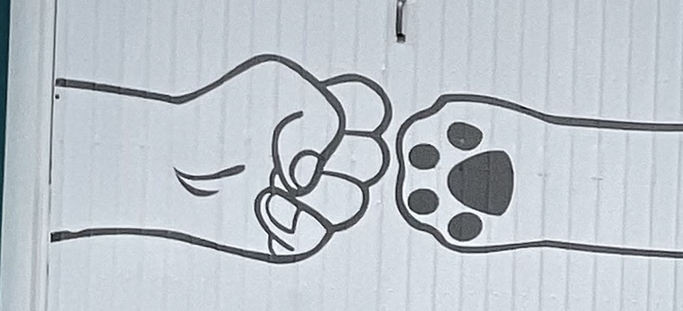 Desenho pintado no portão da clínica: um punho fechado de pessoa encostando numa patinha de animal, como um cumprimento
